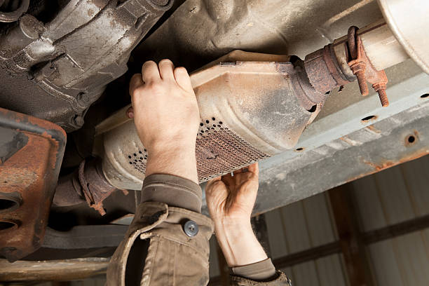Two hands grasp the sides of a catalytic converter under a car.