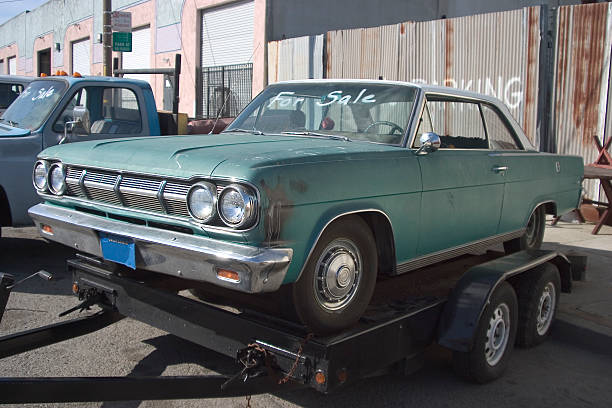 A worn down, teal-colored car sits on a car tow.
